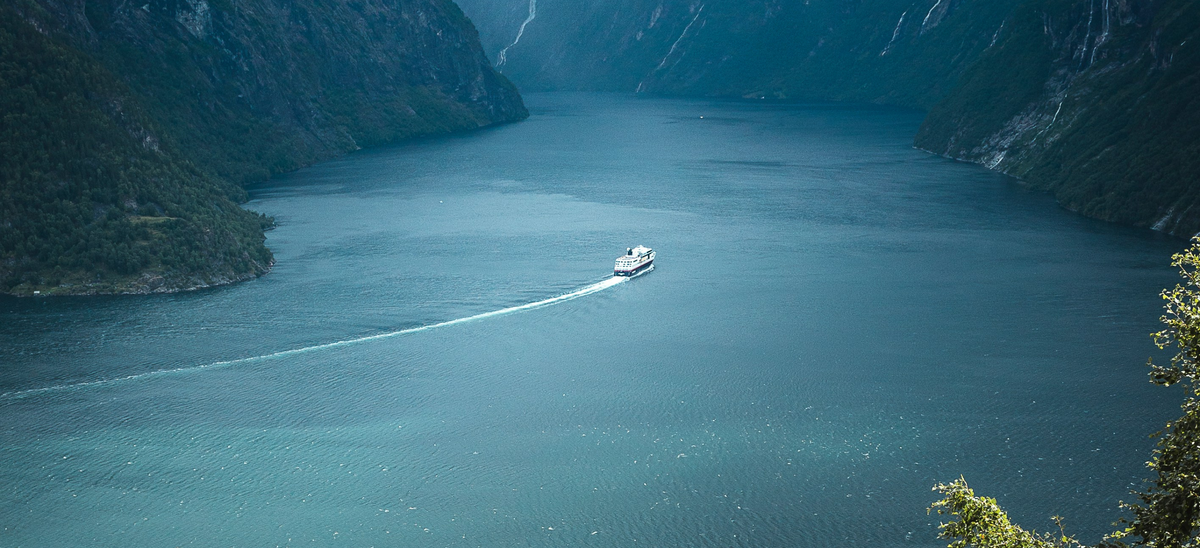 Far out image of a ship traveling through a lake in between mountains.